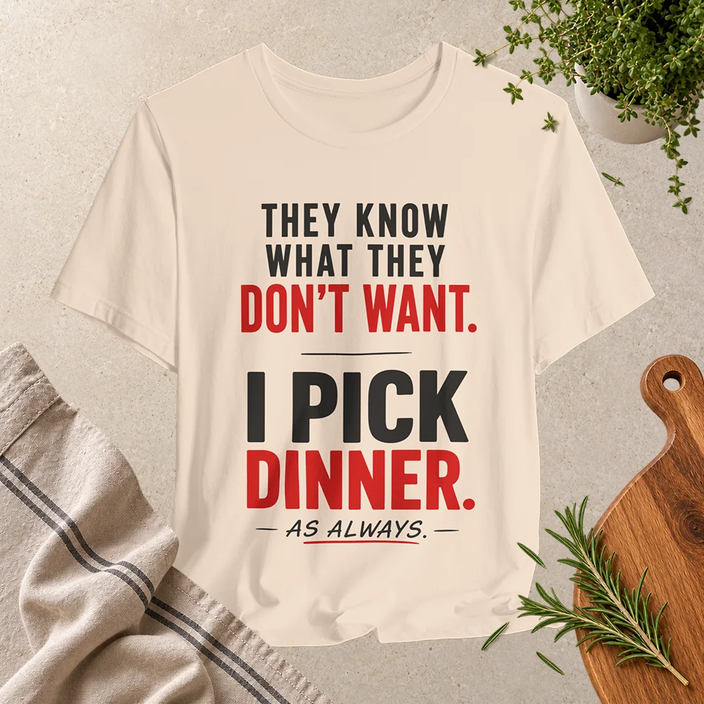 Soft cream T-shirt with bold black and red text reading “They know what they don’t want. I pick dinner. As always.”