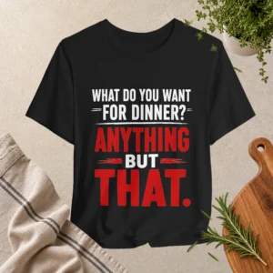 Black T-shirt with the funny dinner quote “What Do You Want for Dinner? Anything But That.” in bold white and red typography, displayed in a kitchen-inspired flat lay setting.